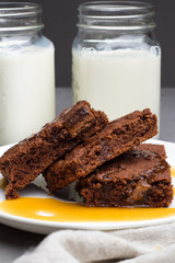 Chocolate brownie with caramel on a white plate, mugs with milk close-up.