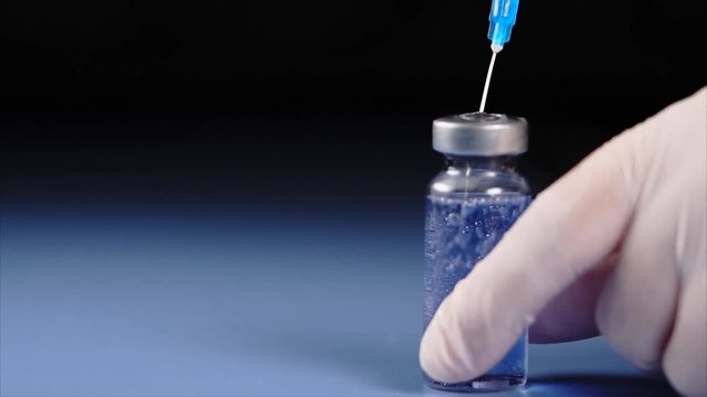 Close up shot mixing of medicine. Syringe squirting fluid into ampoule with blue medicines slow motion.