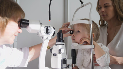 Fototapeta na wymiar Optometrist checks little girl's eyesight - mother and child in ophthalmologist room