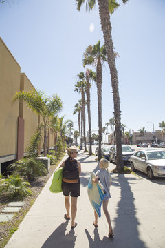 USA, California, San Diego, Woman and girl walking down sidewalk with palm trees along it and carrying surfboards