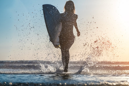 Young woman runs with surfboard with lots of splashes