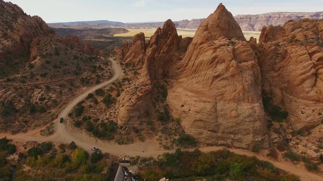 Ascending footage over red rock with vehicle on road in Moab