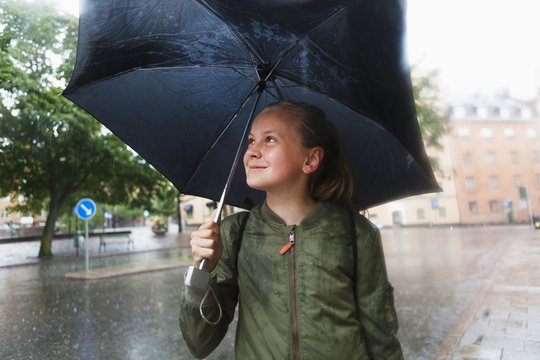 Sweden, Uppland, Solna, Resunda torg, Girl (10-11) carrying umbrella and smiling