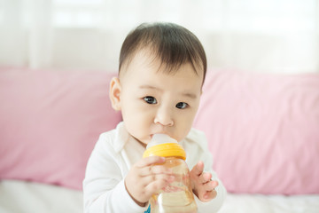 Sweet baby girl sucking milk in bottle at home.