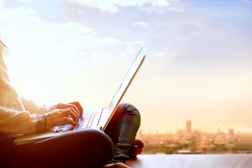 Woman using laptop computer and sitting on the view of a skyscraper with cityscape.