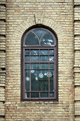 Arched wooden brown window on beige brick wall. White snowflakes are hung inside.