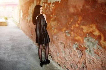 Fotobehang Young goth girl on black leather skirt and jacket against grunge wall. © AS Photo Family