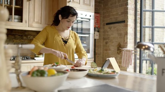  Woman preparing meal in kitchen at home & following recipe on computer tablet