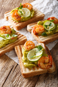 Tasty toast with guacamole, prawns and lime close-up. vertical