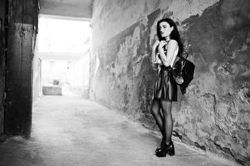 Fototapeta na wymiar Young goth girl on black leather skirt with backpack posed against grunge wall.
