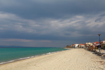 The village on the shore of the turquoise sea under a dark cloudy sky before the rain at sunset of...