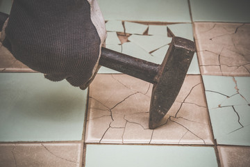 Man's hand with an old iron hammer beating an old tiles. Vintage style. 