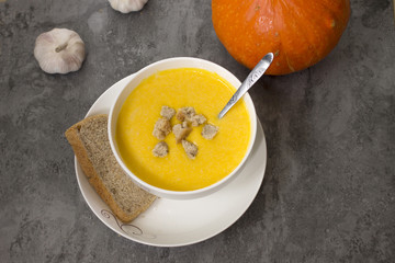 A bowl of pumpkin soup with bread and garlic