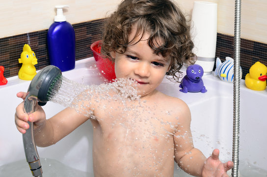 Beautiful Toddler Taking A Bath In A Bathtub With Bubbles. Cute Kid Washing His Hair With Shampoo In The Shower And Splashing Water Everywhere. Boy Playing With Toys In The Tub