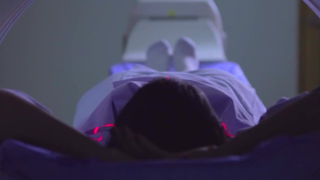 Woman in a blue patient gown into a tomography machine