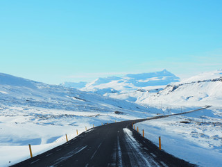 Winter road with mountain on the side of the road covered with snow. Sunny day and clear blue sky