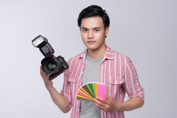 Young asian photographer holding digital camera and color checker card and color palette, while...