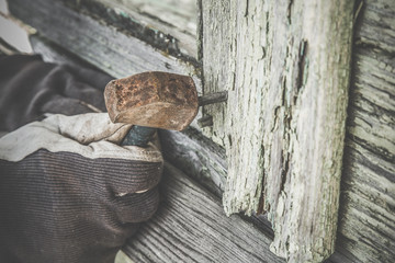 Carpenter's hand in protective glove in the wooden boards beating nail with a small, old iron hammer. Old rural home repair. Countryside. Vintage style.