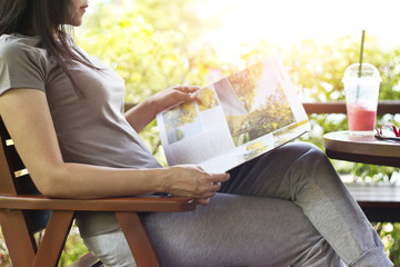 woman relaxing by reading travelling magazine and strawberry smoothie on table, nature background