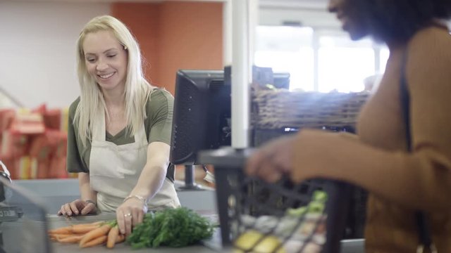  Grocery store worker scanning & packing customer's shopping at the checkout