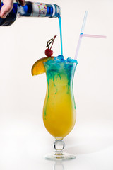 Preparing an exotic cocktail to pour blue syrup into orange juice
