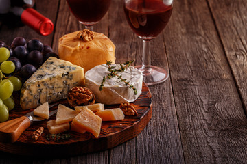 Cheese, nuts, grapes and red wine on wooden background.