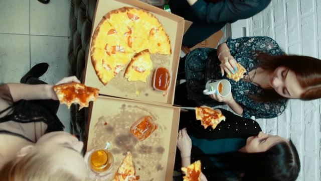 Group of young happy women eating pizza, laughtering and smiling in room with white brick wall, girlfriends enjoy time together, overhead view.