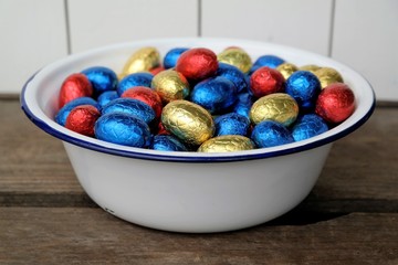 chocolate Easter eggs, red, blue and yellow, together in a enamel bowl, taken from above