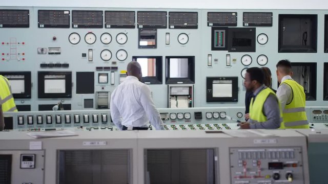 Workers in power plant control room looking at control panel & checking system