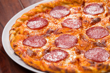 Top view of pizza with salami on a wooden background