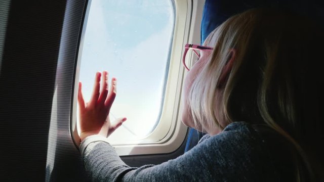 A 6-year-old girl with spectacles sits in a plane, looks out the window. Her hand is pressed to the porthole - a happy journey