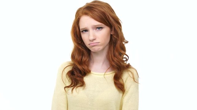 Sad disappointed young woman with long red hair showing thumbs down over white background