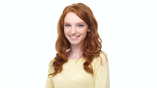 Smiling confident young woman with long red hair pointing two fingers at camera isolated over white background