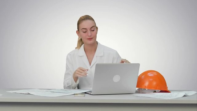 Tired young woman in safety helmet yawning and try to work on white background.