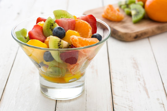 Fruit salad in crystal bowl on white wooden table.
