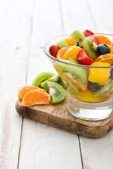 Fruit salad in crystal bowl on white wooden table.
