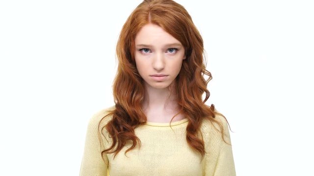 Frustrated upset young woman with red hair looking at camera isolated over white background