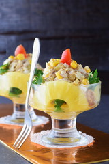 Salad with chiken fillet, pineapple, mushrooms, walnuts in a glass dish on a grey abstract background. Healthy eating concept. Russian traditional food