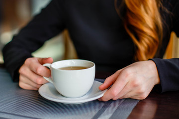 Closeup of women's hands with green tea mug while sitting in comfortable cafe.