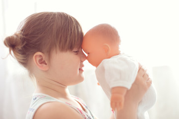 Girl kid cares about a doll, close-up, lifestyle