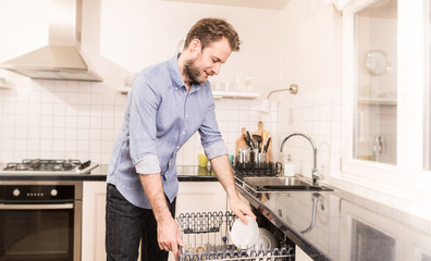 Man loading dishwasher machine in the home kitchen