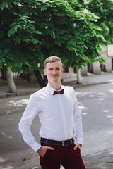 Close-up portrait of a young handsome guy groom delectable hipster in a suit and bow tie on a background field smiling and posing  