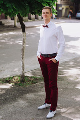Close-up portrait of a young handsome guy groom delectable hipster in a suit and bow tie on a background field smiling and posing  