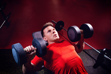 A sporty blond man doing exercises with dumbbells in the gym.