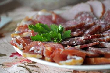 Different smoked sausages and meat decorated with parsley on a plate on a festive table close up.