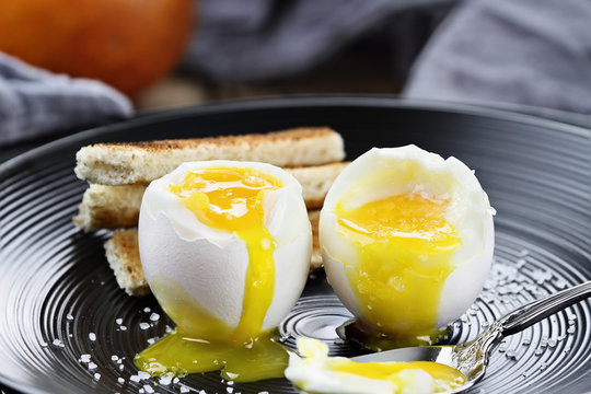 Two soft boiled eggs with toast soldiers and fruit in the background. Extreme shallow depth of field with selective focus.