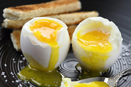 Two soft boiled eggs with toast soldiers in the background. Extreme shallow depth of field with selective focus.