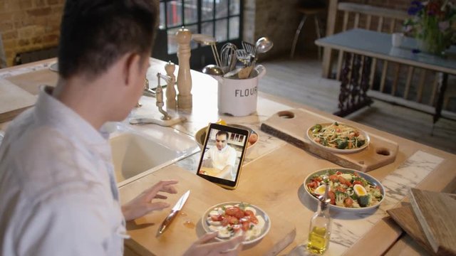  Young man watching cookery show on computer tablet & following recipe