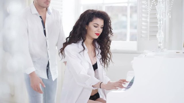  Couple in elegant apartment, woman playing piano in just lingerie & shirt