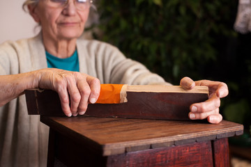 elderly woman restoring her furniture using a sanding paper